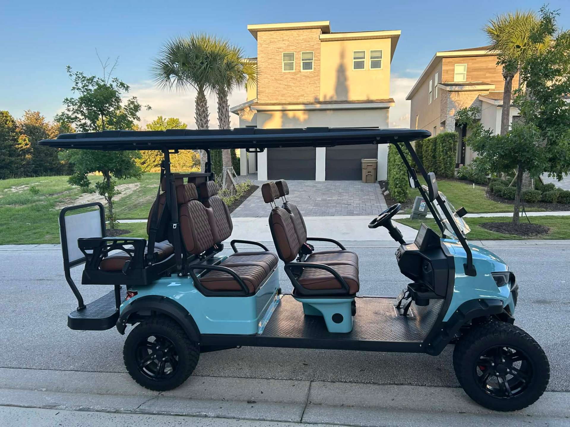 Side view of teal 6-seater luxury golf cart parked at a Reunion Resort vacation home at golden hour